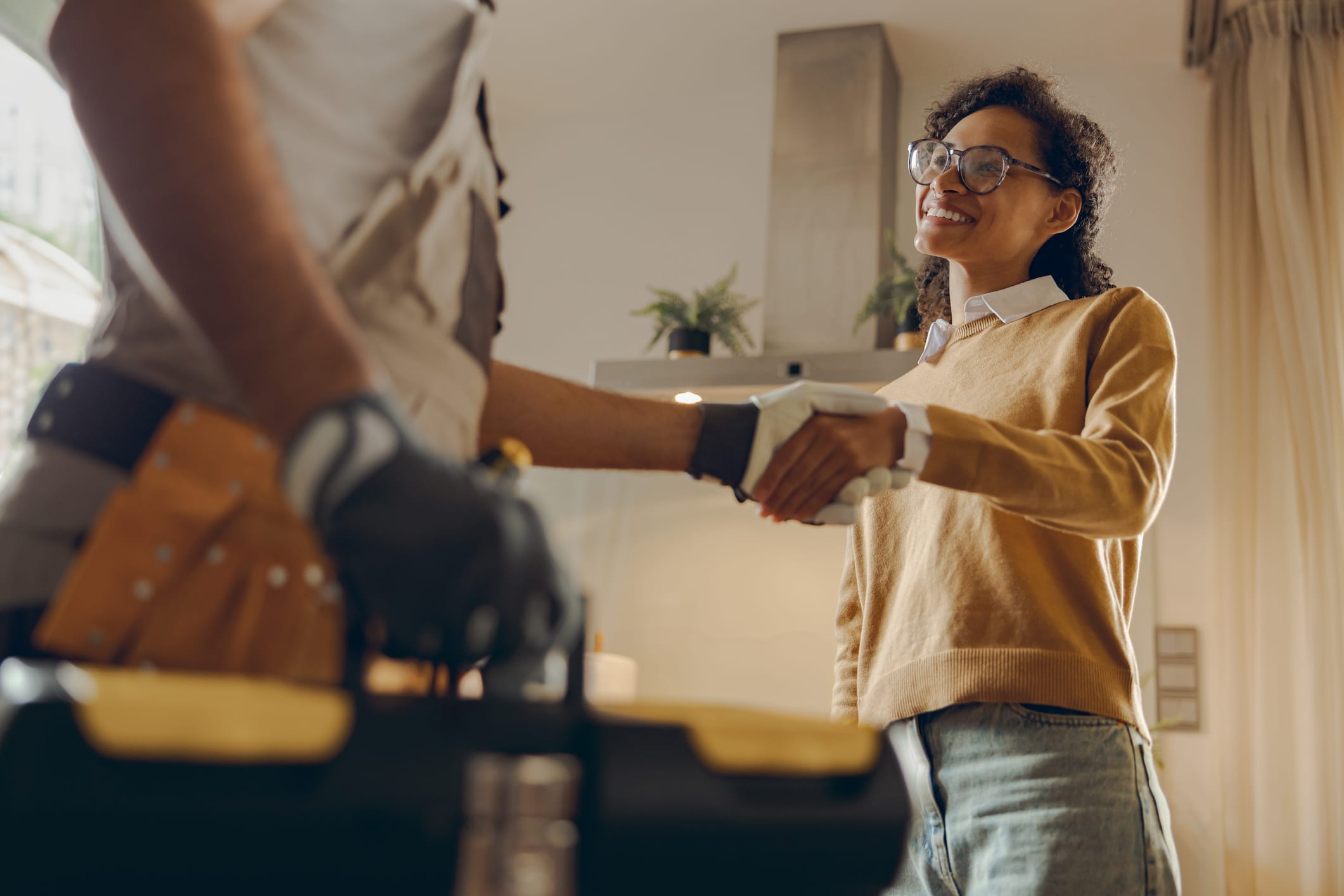 Home close up of male handyman shaking hands with happy female client while standing at home kitchen